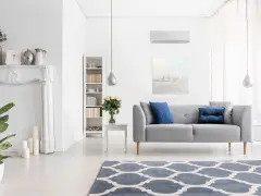 Nowoczesny salon z klimatyzacją w trybie funkcja dry, szara kanapa, kominek, regał i dywan.