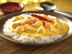 Straccetti di pollo al curry su un letto di riso bianco, guarniti con peperoncino rosso fresco. Un piatto invitante e saporito.