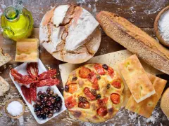 Apulia jedzenie: świeże pieczywo, focaccia z pomidorami, oliwki, suszone pomidory i oliwa z oliwek na drewnianym stole.