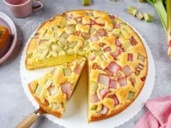 Saftiger Rhabarberkuchen, ein Klassiker unter den Rezepten mit Rhabarber. Ein Stück wird gerade herausgehoben.