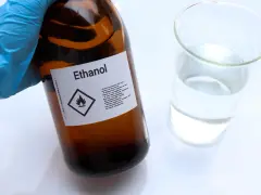 Braune Glasflasche mit der Aufschrift "Ethanol" und einem Warnsymbol. Daneben ein Becherglas mit klarer Flüssigkeit. Hier gibt es 100 prozentigen Alkohol.