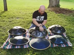 Mann spielt auf mehreren runden Metallinstrumenten im Freien.