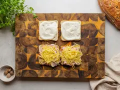 Przygotowanie croque madame: na kromkach chleba szynka i ser, na drugiej sos beszamelowy.