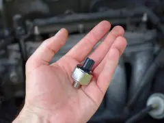 A hand holds a new oil pressure sensor, a potential fix for a p0332 code Chevy Silverado.