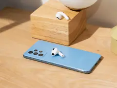 AirPods liegen auf einem blauen Samsung-Smartphone und einem Holzblock.