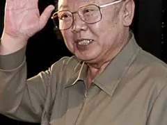 Kim Jong Il w okularach, machający ręką.