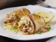 Deliziosi involtini di pesce spada ripieni, serviti su un piatto bianco con spicchio di limone e prezzemolo tritato.