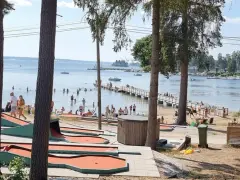 Minigolfbana vid Engesbergs camping. Många badar och solar vid vattnet, en brygga leder ut i sjön.