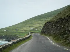 A winding road along the coast of Ireland, perfect for renting a car and exploring the dramatic green hills and stone walls.