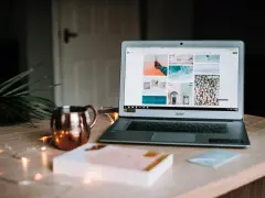 Laptop z otwartym portfolio zdjęć na ekranie, obok miedziany kubek i ozdobne lampki.