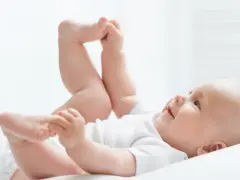Uśmiechnięte dziecko leży na plecach, podnosząc nóżki. Czas na zmianę pampersów na większe, gdy maluch rośnie.