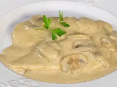 Pollo cremoso con champiñones y perejil en un plato blanco.