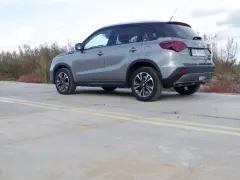 Szary Suzuki Vitara Hybrid z czarnym dachem stoi na betonowej nawierzchni z żółtymi pasami.