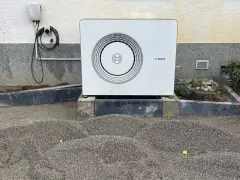 Unité extérieure d'une chaudière à condensation Bosch, installée sur des blocs de béton, avec un chargeur mural à proximité.
