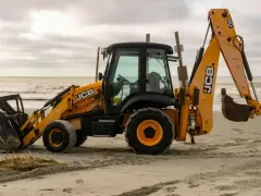 Żółta koparko-ładowarka firmy JCB stoi na piaszczystej plaży, gotowa do pracy.