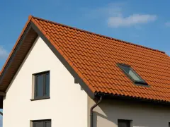 Ceglasty dach dwuspadowy z dachówką ceramiczną i oknem połaciowym. Kąt nachylenia dachu jest umiarkowany, idealny do odprowadzania wody.