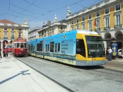 Lizbona tramwaj: nowoczesny, niebiesko-żółty pojazd obok zabytkowego, czerwonego tramwaju na tle żółtych budynków.
