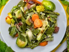 Menestra de verduras variadas con trozos de jamón en un plato blanco.