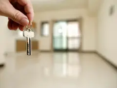 Mano sosteniendo una llave plateada frente a una habitación vacía y desenfocada.