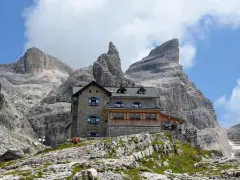 Il rifugio Tuckett e Sella, un'oasi di pietra tra le imponenti vette dolomitiche, accoglie escursionisti sotto un cielo azzurro e nuvoloso.
