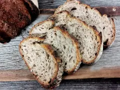 Ein Laib Sauerteigbrot, angeschnitten, mit sichtbarer, knuspriger Kruste. Die Scheiben zeigen eine luftige Krume. Hoffentlich ist die brotkruste zu hart, um sie zu genießen.