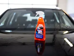 En flaska SONAX Xtreme Wet Coat står på en våt, mörk bilhuv.