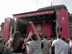 Menschen jubeln bei einem Open-Air-Konzert vor einer Bühne mit Sparkassen-Logo.