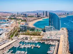 Barcelona morze: luksusowe jachty w marinie, plaża pełna ludzi i nowoczesny hotel w kształcie żagla.