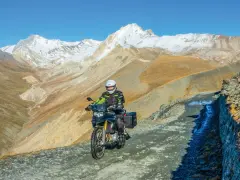 Un motociclista avventuroso affronta un sentiero impervio con la sua jafferau moto, circondato da maestose montagne innevate e paesaggi aridi.