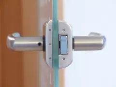 Metalowa zasuwa w szklanych drzwiach, z uchwytami po obu stronach.
