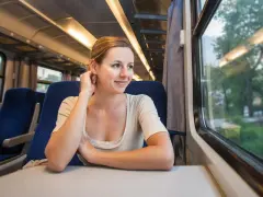 Uśmiechnięta kobieta podróżuje pociągiem, podziwiając krajobrazy, które mogą być częścią najpiękniejszych tras kolejowych w Europie.