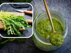 Un mazzetto di rucola fresca su un tagliere e un barattolo pieno di vibrante pesto di rucola, pronto per insaporire i tuoi piatti.