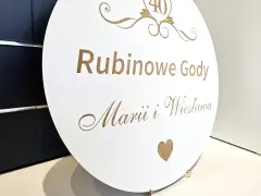 Okrągła tablica z napisem "Rubinowe Gody Marii i Wiesława" i cyfrą "40" upamiętnia 40 rocznicę ślubu.