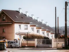 Rząd domów tworzy spójną zabudowę szeregową. Jasne fasady, ciemne dachy i białe kominy tworzą harmonijną całość.