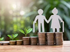Figuras de papel de ancianos sobre pilas de monedas y brotes verdes. ¿Es sostenible el sistema de pensiones en España?