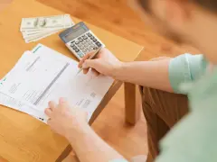 Persona revisa documentos y billetes, calculando cómo hacer un recibo de pago.
