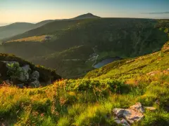 Słoneczny poranek w Karkonoszach. Widok na górzyste tereny, lasy, jezioro i charakterystyczny szczyt.