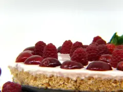 Cheesecake senza gelatina, guarnita con lamponi succosi e ciliegie lucide, su una base croccante.