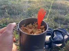 Un repas simple pour savoir que manger en randonnée : des pâtes avec des olives dans une tasse de camping, avec une fourchette orange.