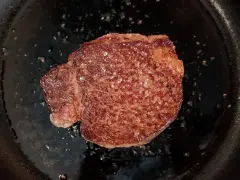 Ein saftiges Steak brutzelt in der Pfanne, bestreut mit grobem Salz.