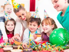 Glada barn med kalas-hattar firar ett kalas för en 2-åring med muffins och ballonger.
