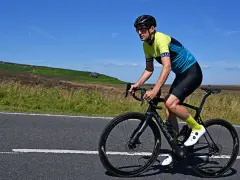 Man cycling on max speed on a scenic road with hills in the background.