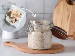 Ein Glas mit blubberndem Sauerteig, daneben frische Hefe. Die Frage: wie lange muss sauerteig gehen?