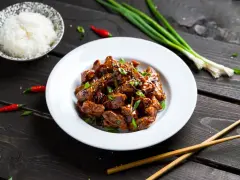 Pyszny kurczak luc lac w sosie, posypany szczypiorkiem i sezamem, obok miseczka ryżu, pałeczki i papryczki chili.
