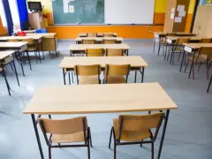 Pusta klasa szkolna z rzędami ławek i krzeseł. W tle tablica i okna. Obowiązek nauki czeka na uczniów.