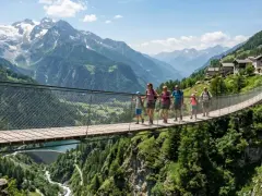 Famiglia attraversa un suggestivo ponte tibetano in Lombardia, con montagne innevate e un villaggio alpino sullo sfondo.
