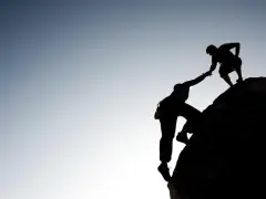 Silhouette d'un grimpeur aidant un autre à atteindre le sommet. Une belle présentation photographe de l'entraide et de la persévérance.