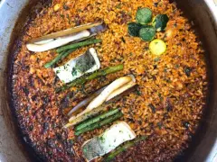 Deliciosa paella valenciana con arroz dorado, espárragos, pescado y navajas.