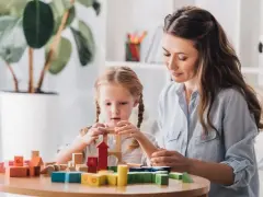 Kobieta i dziewczynka budują wieżę z kolorowych klocków.