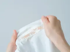 Dłonie trzymają białą koszulę z widoczną, **starą plamą z podkładu** na kołnierzyku.